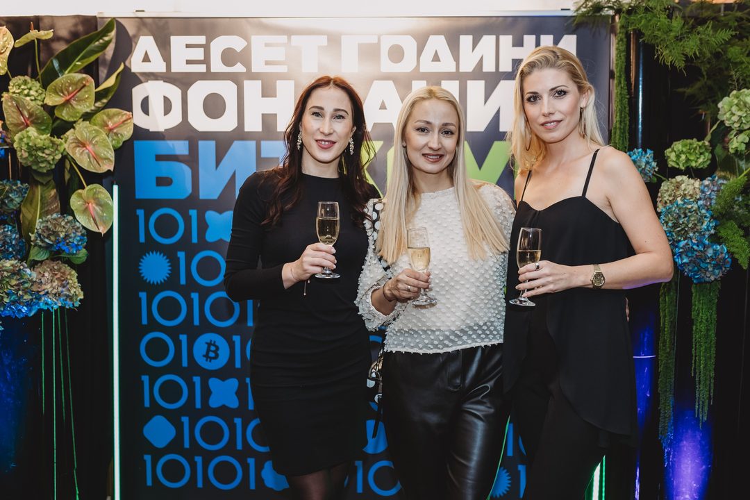 Three guests pose with champagne in front of the Bithope Foundation 10-year anniversary photo wall in Sofia.