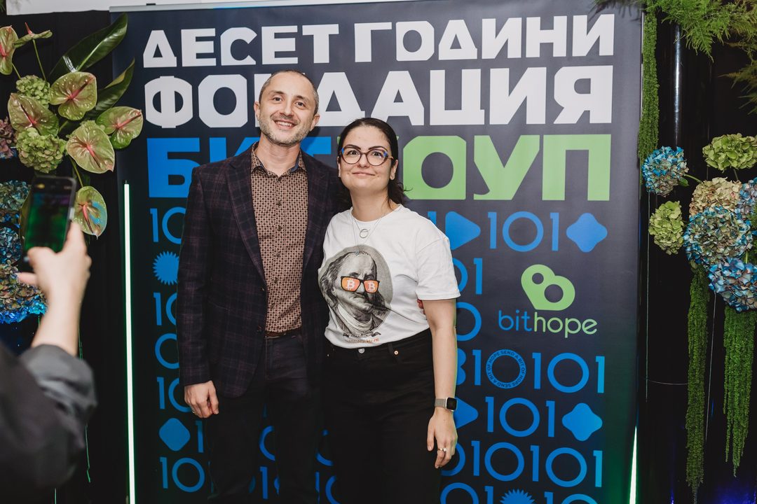 Founder Vladislav Dramaliev with a bitcoin-enthusiast supporter in front of the Bithope Foundation 10-year anniversary photo wall.